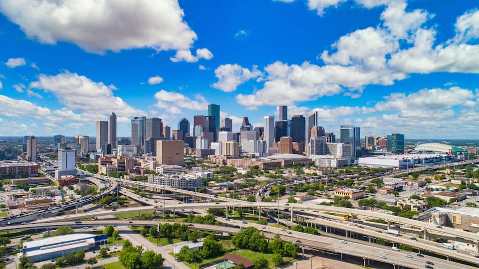 A city skyline with modern skyscrapers, a highway system, and a stadium.