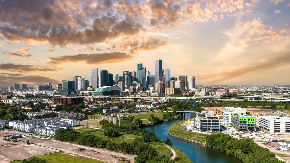 A city skyline with modern skyscrapers, a river, and surrounding greenery.