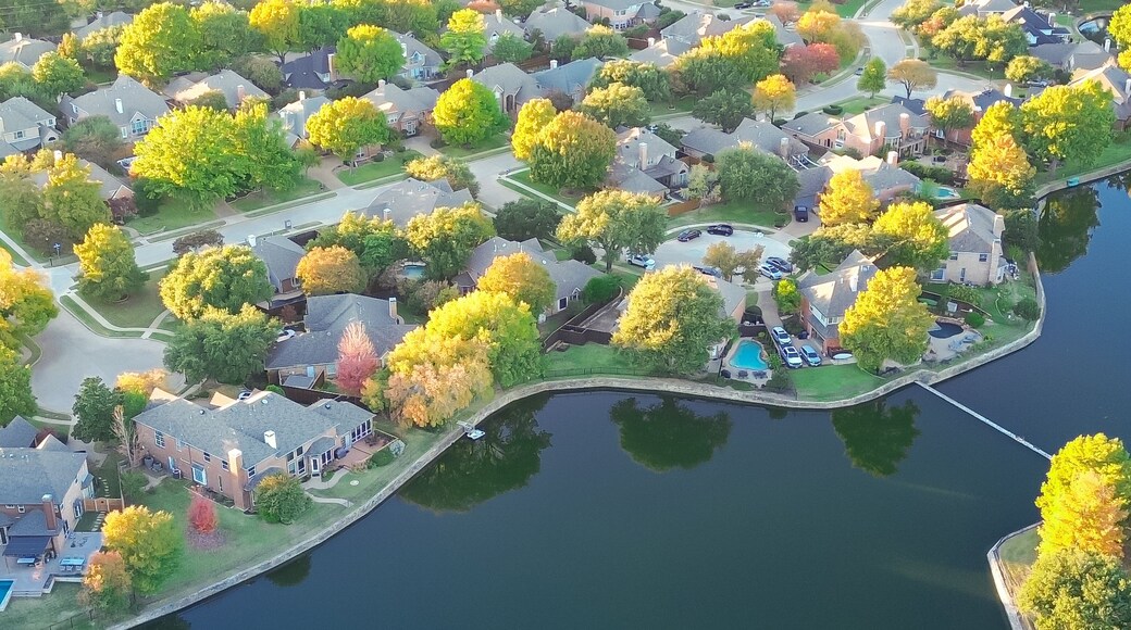 An aerial view of a residential area with houses, a lake, and autumn-colored trees.