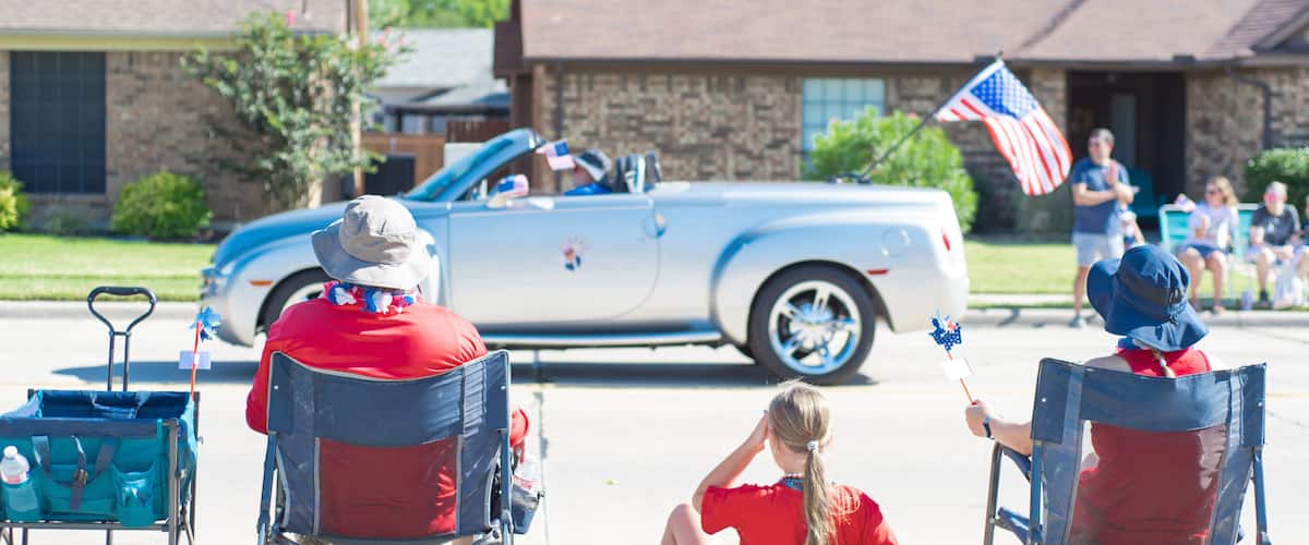 A vintage convertible car, two people in wheelchairs, and a residential street with houses.