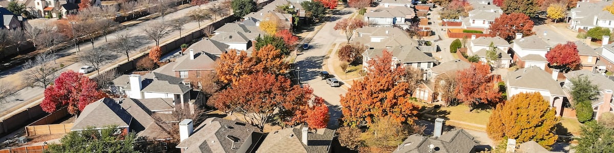 Panorama top view beautiful neighborhood in Coppell, Texas, USA in autumn season. Row of single-family home with attached garage, garden, surrounded by colorful fall foliage leaves under blue sky