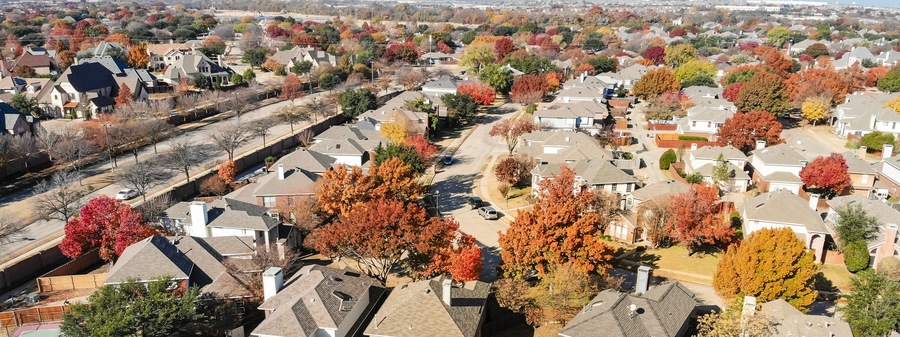 Panorama top view beautiful neighborhood in Coppell, Texas, USA in autumn season. Row of single-family home with attached garage, garden, surrounded by colorful fall foliage leaves under blue sky