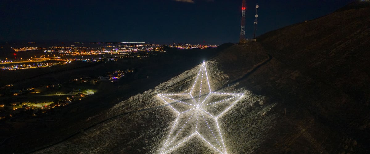 A star-shaped light installation on a hill with a cityscape in the background.