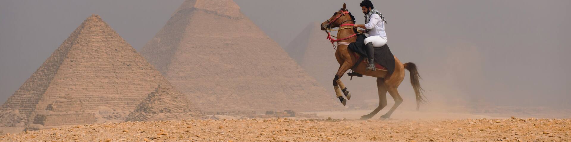 A person riding a horse in front of the Great Pyramids of Giza.