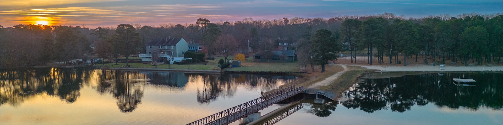 Un lac paisible, avec un pont en bois, des maisons et des arbres en arrière-plan.