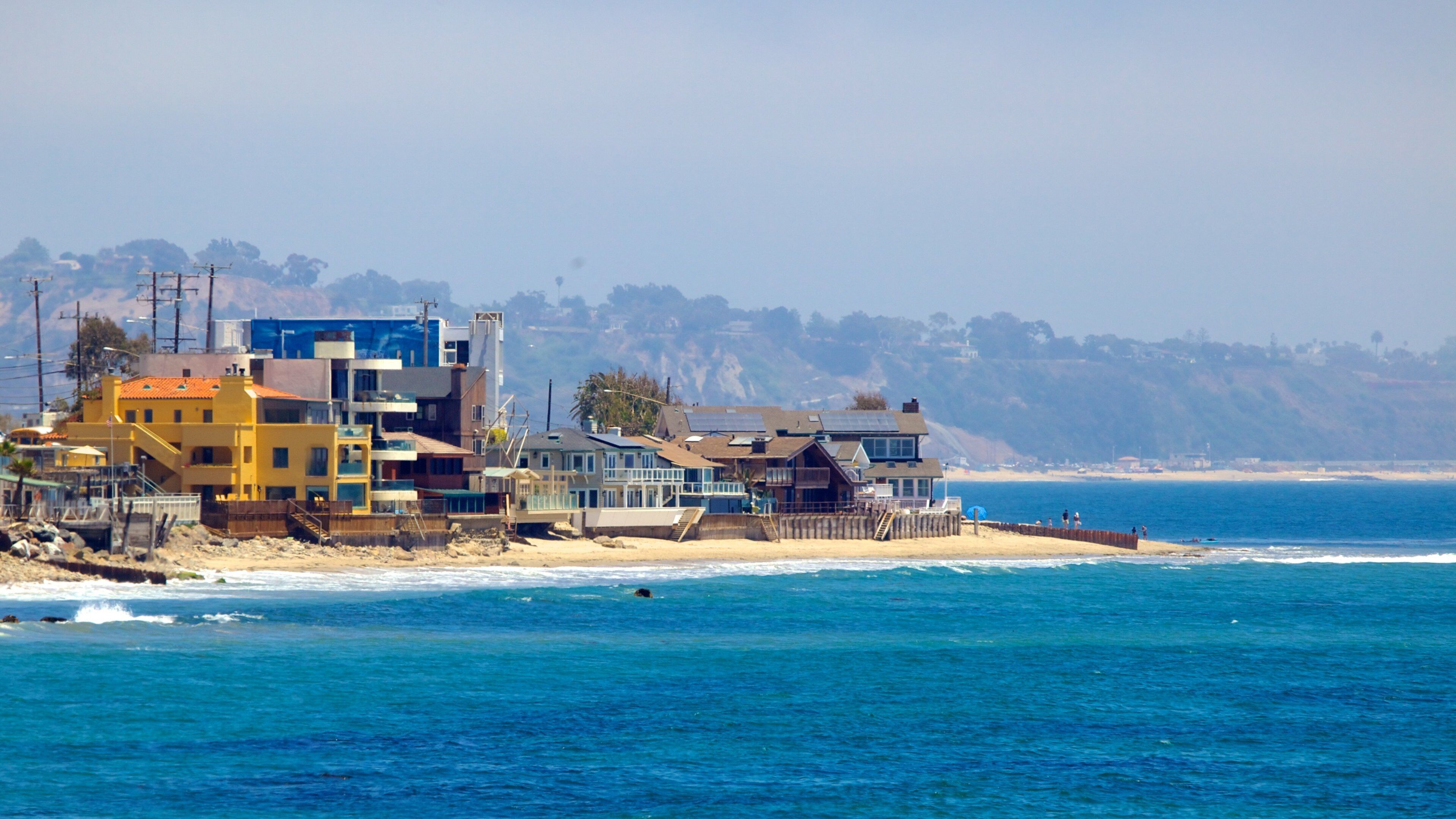 A coastal residential area with houses near the beach and cliffs in the background.