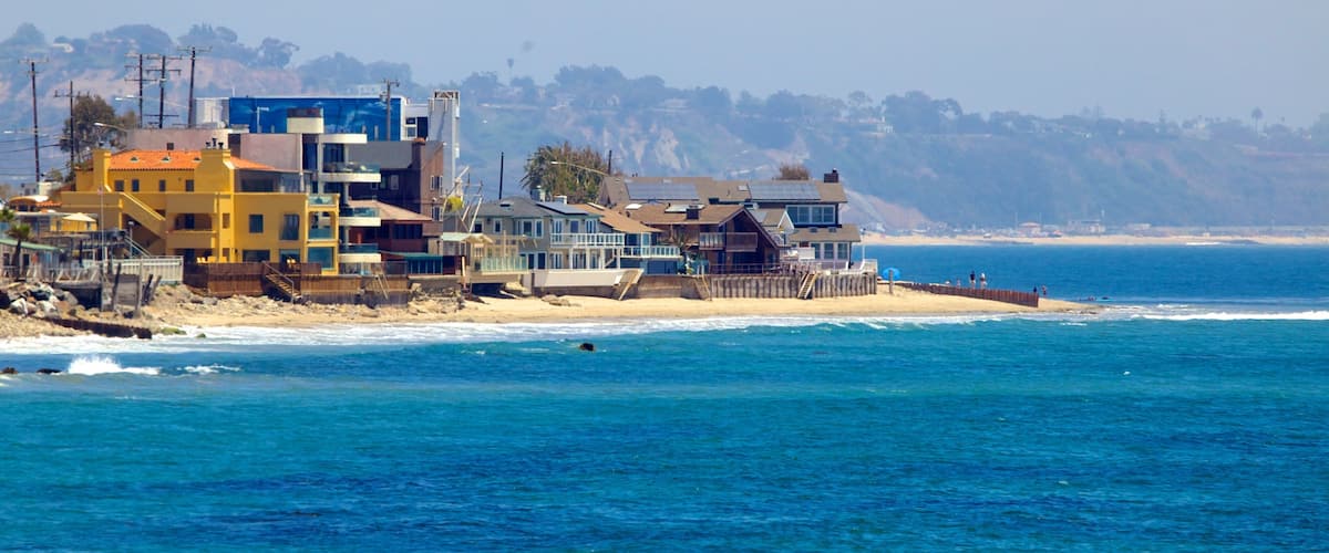 A coastal residential area with houses near the beach and cliffs in the background.