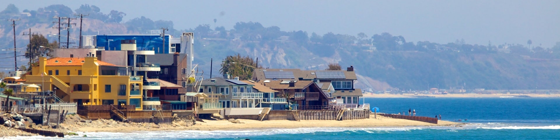 A coastal residential area with houses near the beach and cliffs in the background.