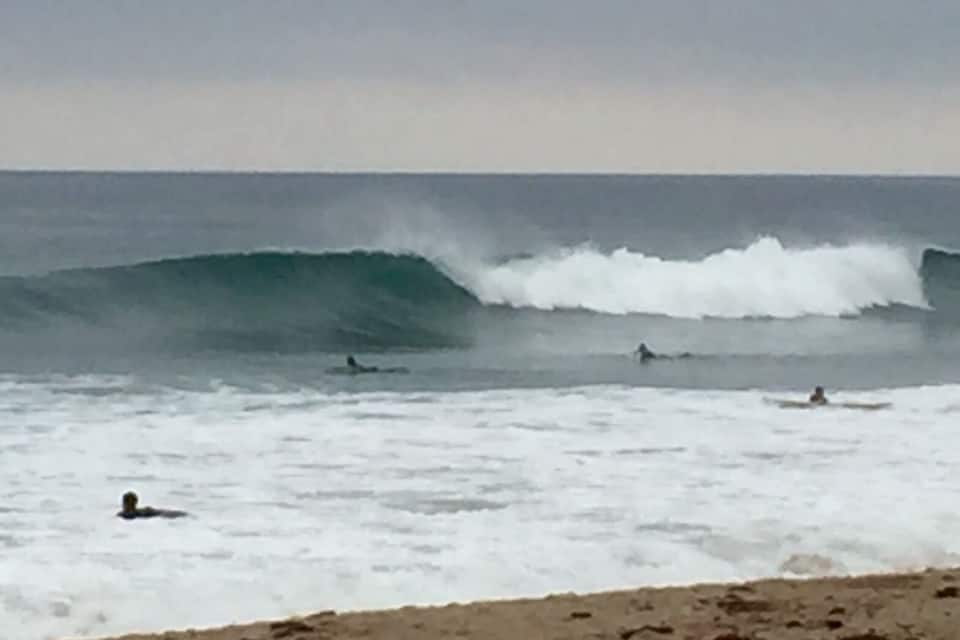 A beach with large waves and surfers.