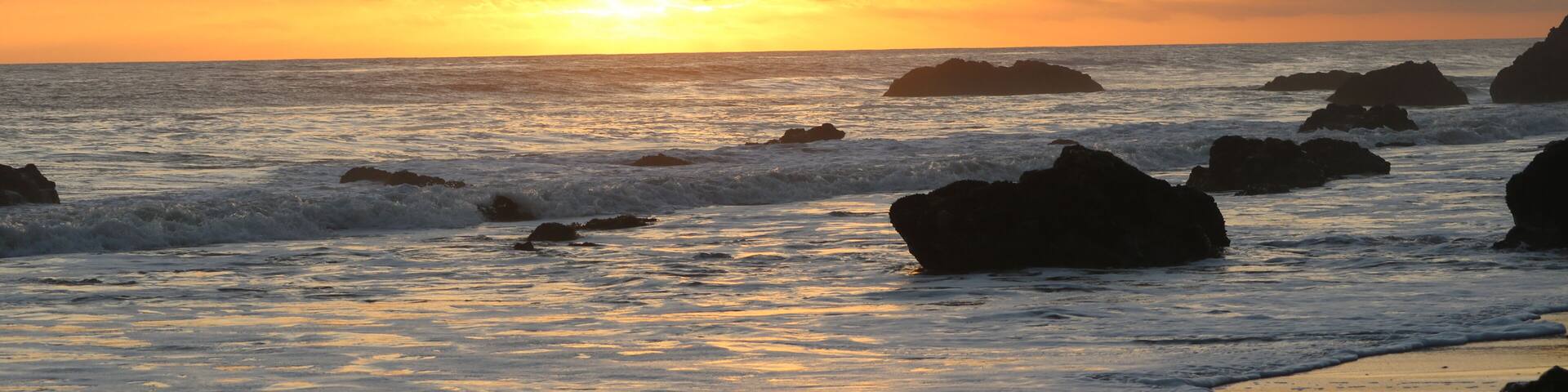Un atardecer sobre una playa rocosa con olas rompiendo contra las rocas.