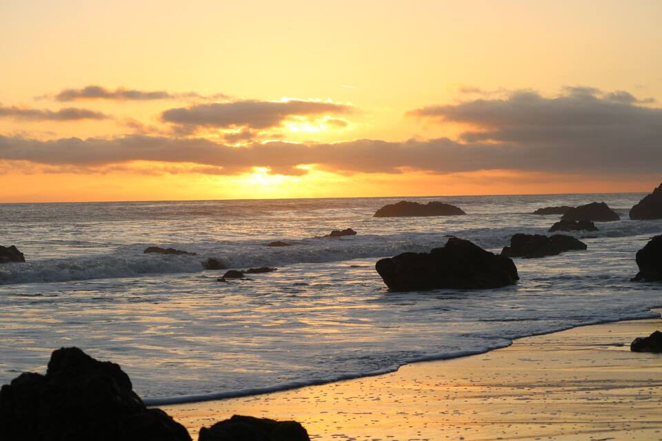 A sunset over a rocky beach with waves crashing against the rocks.