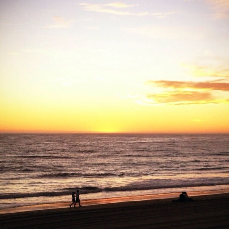 Una playa al atardecer con dos personas caminando y un perro en la arena.