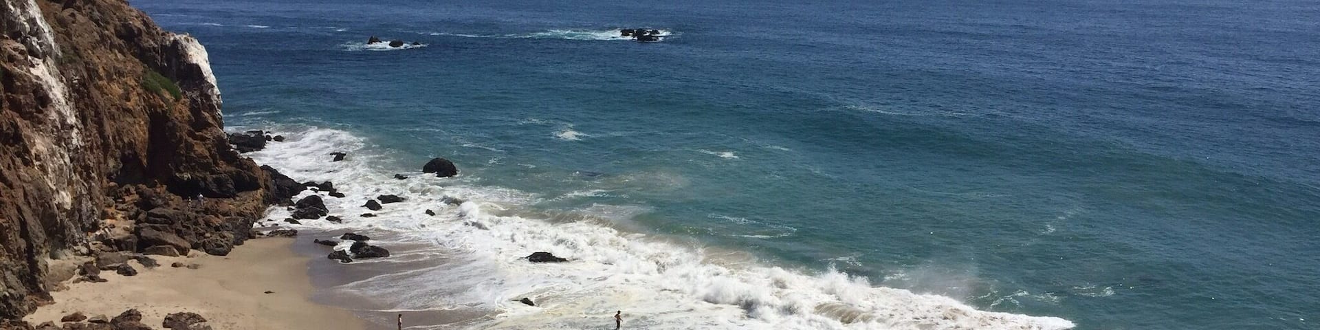 A coastal beach with rocky cliffs and waves crashing onto the shore.