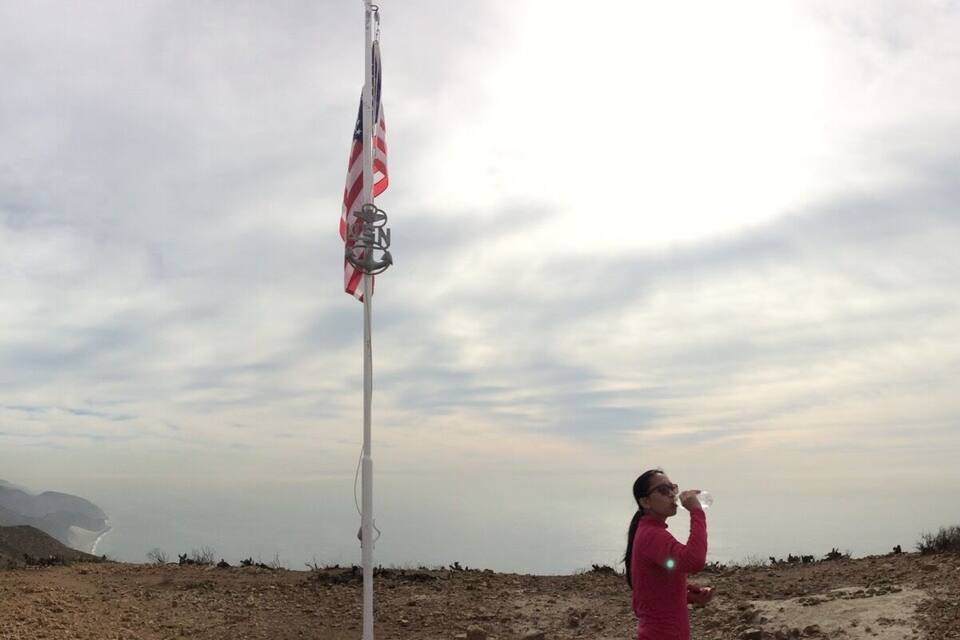 A flagpole with an American flag, a person drinking water, and a mountainous landscape in the background.
