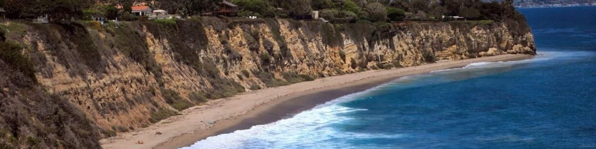 Un paisaje costero con una playa de arena, acantilados y un océano azul claro.