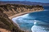 A coastal landscape with a sandy beach, cliffs, and a clear blue ocean.