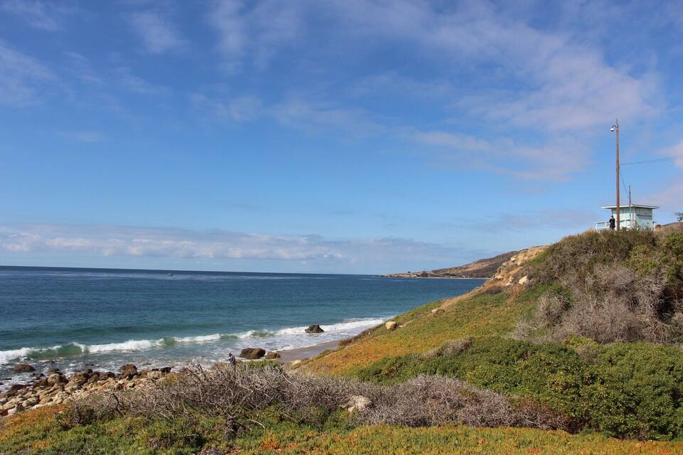 A coastal landscape with a lighthouse, rocky shoreline, and grassy hills.