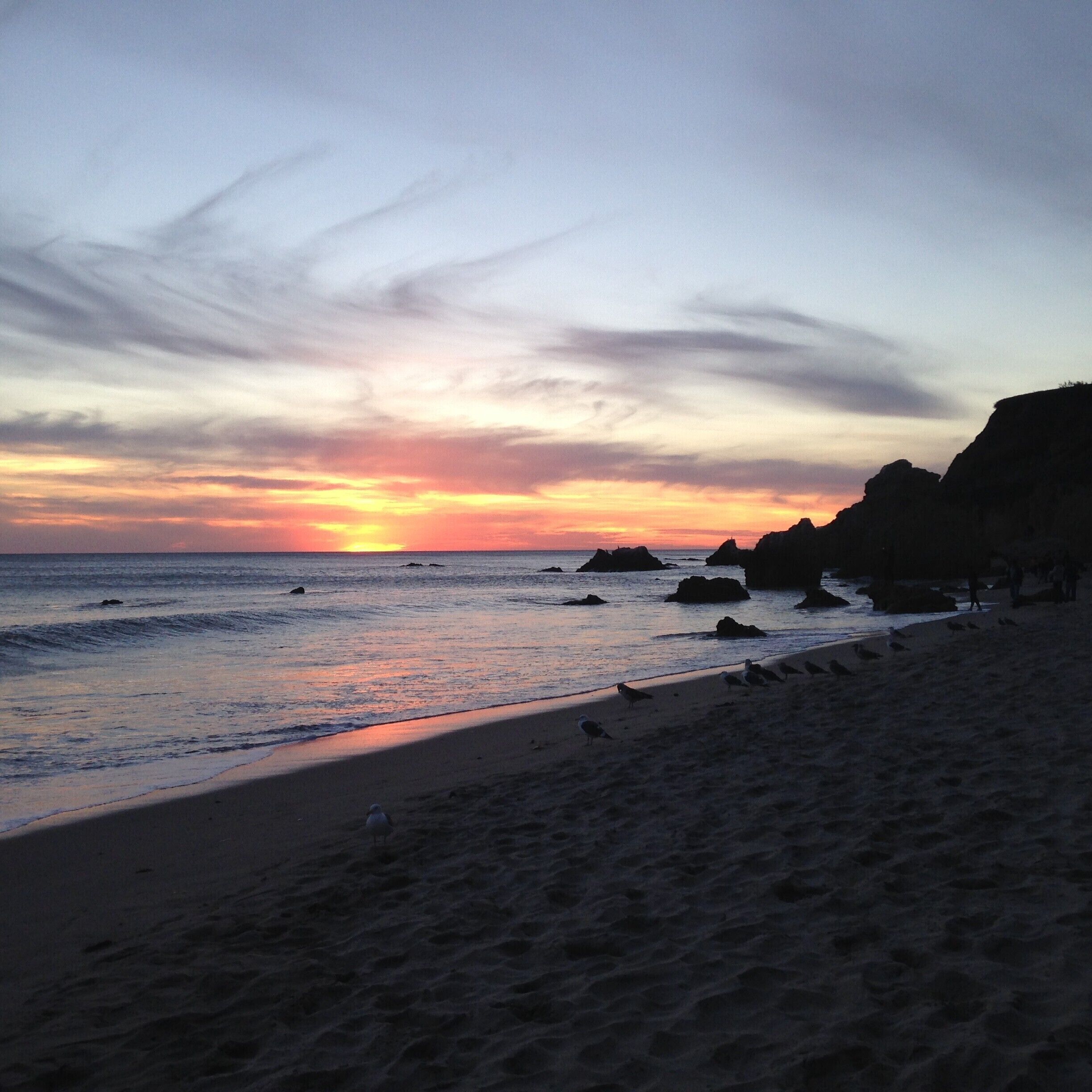 A beach at sunset with rocky outcrops and waves.