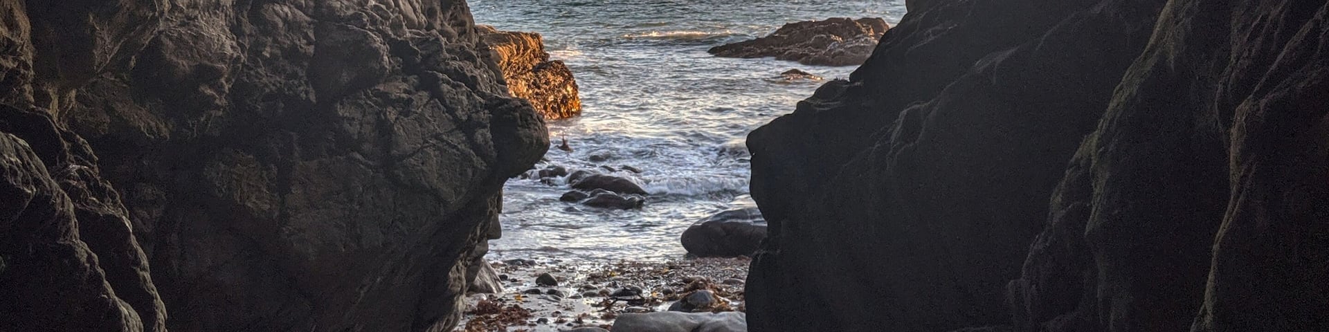 A rocky cave opening to a beach with waves and a sunset.