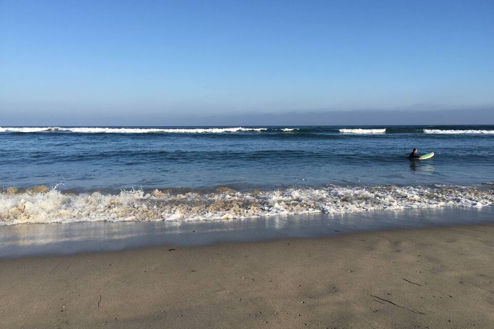 A beach with waves and a surfer in the water.