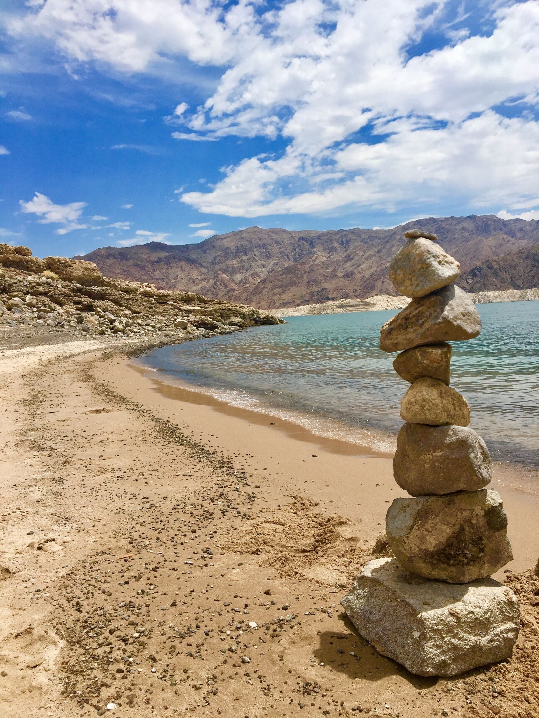 A stack of rocks on a beach with mountains in the background.