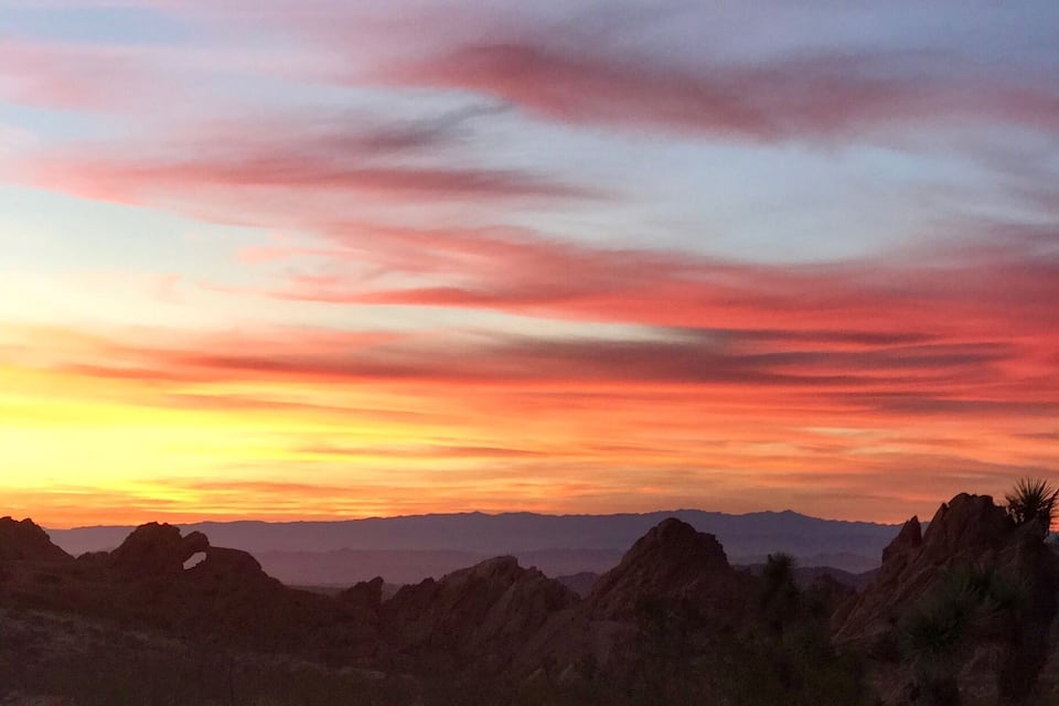 A desert landscape with rocky formations and a colorful sunset sky.