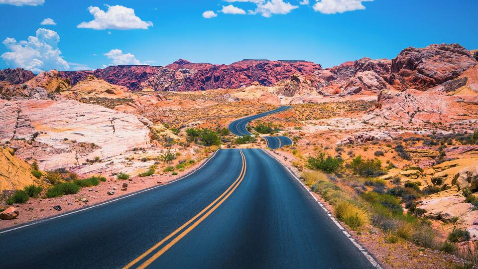 A winding road through a desert landscape with red rock formations and sparse vegetation.