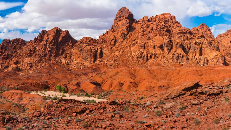 A rugged desert landscape with prominent red rock formations and a winding dirt path.