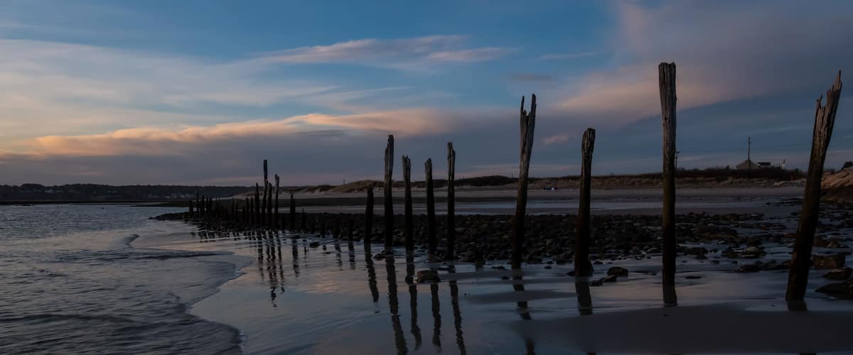 Une plage avec des poteaux en bois et des eaux calmes qui reflètent le ciel.