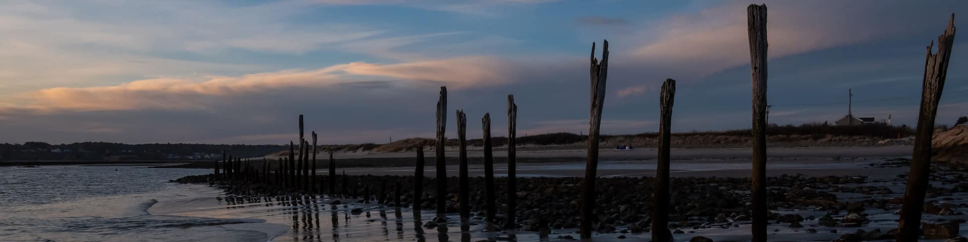 A beach with wooden posts and calm waters reflecting the sky.