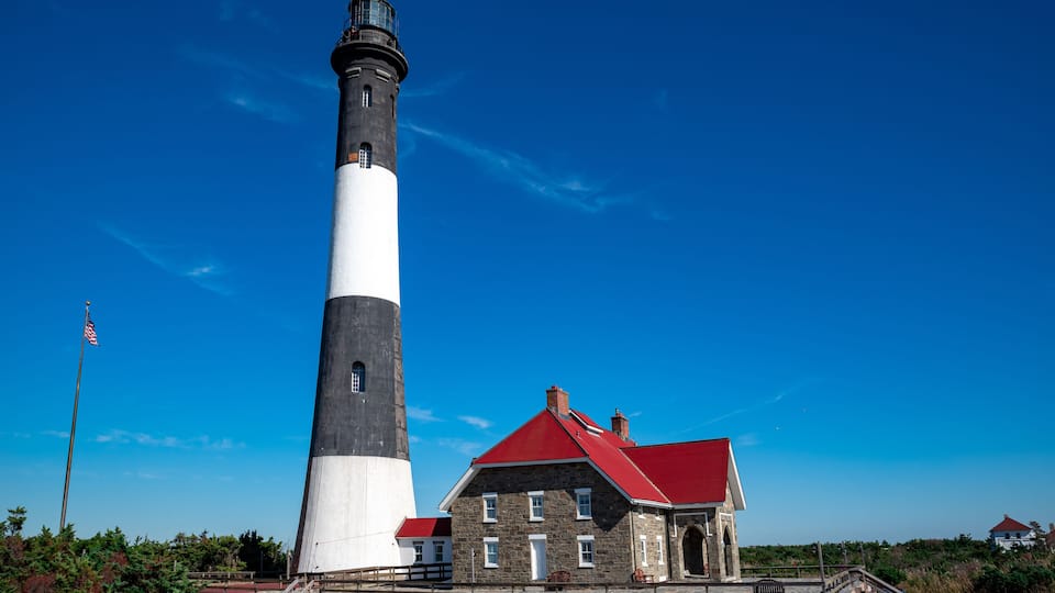 A lighthouse with a red roof, a stone building with a red roof, and an American flag.