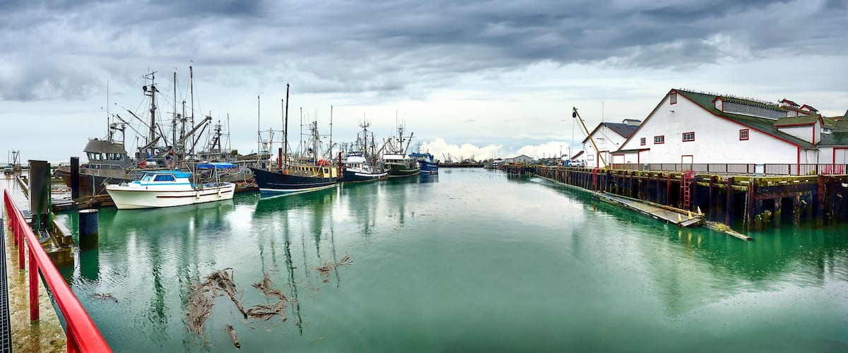 A harbor with several fishing boats docked, a red bridge, and a white building with a red roof.