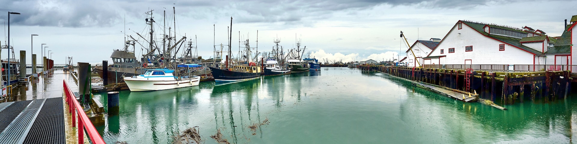 A harbor with several fishing boats docked, a red bridge, and a white building with a red roof.
