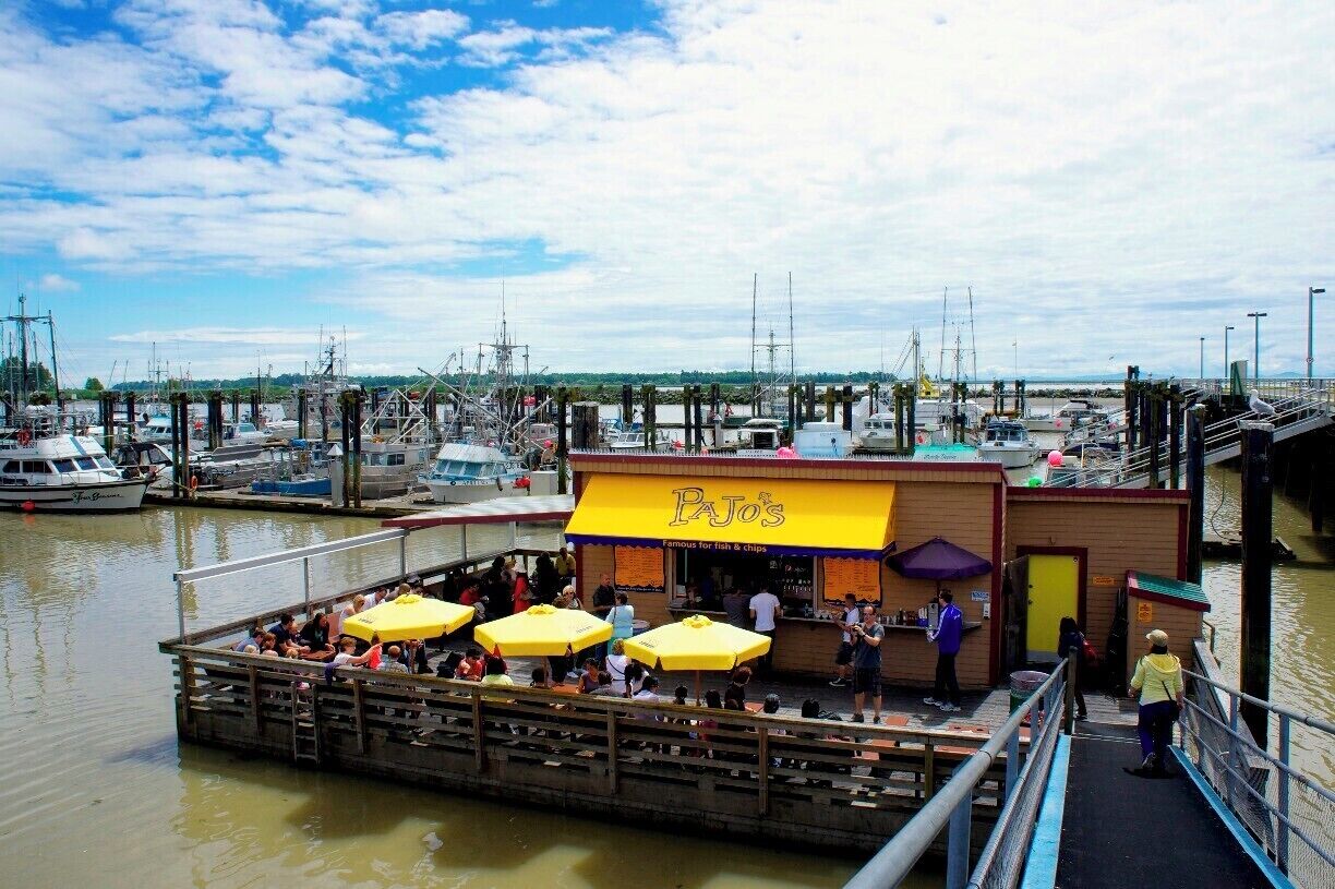 Um restaurante à beira-mar chamado PAJO'S, com mesas ao ar livre e vista para barcos e cais.