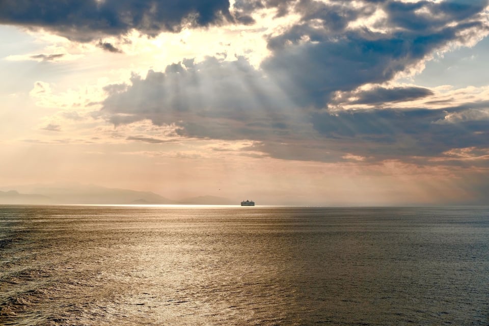A ship on a calm sea with a sunset and clouds in the background.