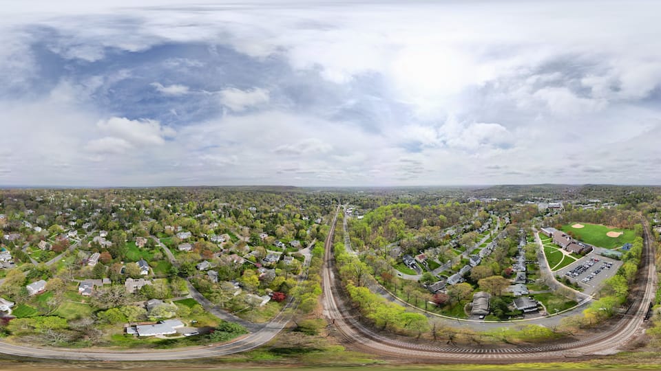 A panoramic view of a suburban area with a railway track, residential houses, and green spaces.