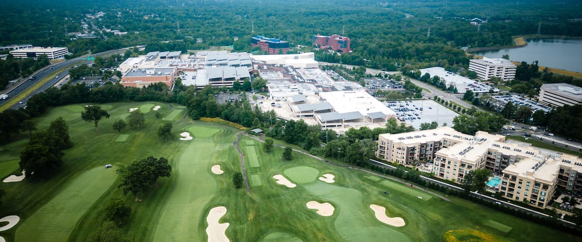 An aerial view of a golf course with sand bunkers, surrounded by buildings and roads.