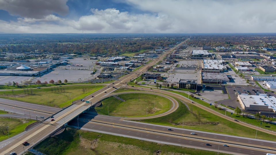 An aerial view of a city with a highway, industrial buildings, and a large green park area.