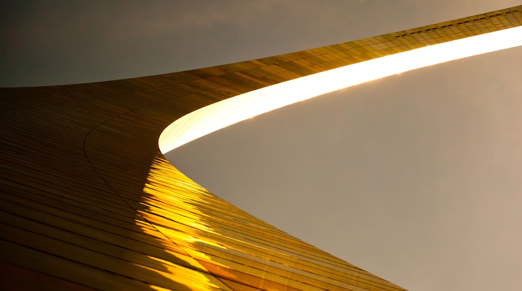 A curved architectural structure with a reflective surface, possibly a modern building or pavilion, under a cloudy sky.