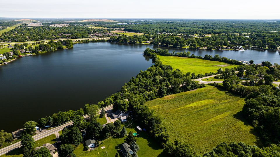 A large lake surrounded by lush greenery, residential areas, and a highway.