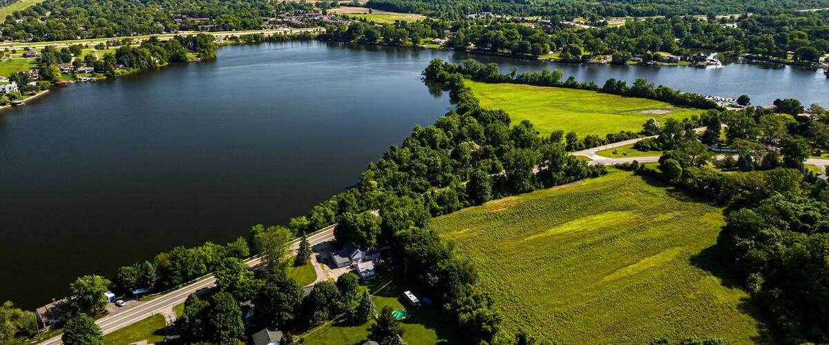 A large lake surrounded by lush greenery, residential areas, and a highway.