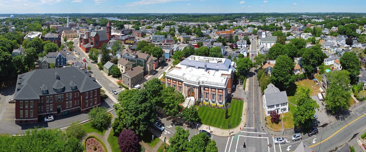 An aerial view of a town with a prominent red brick building, a church with a steeple, and a large white building with a dome.