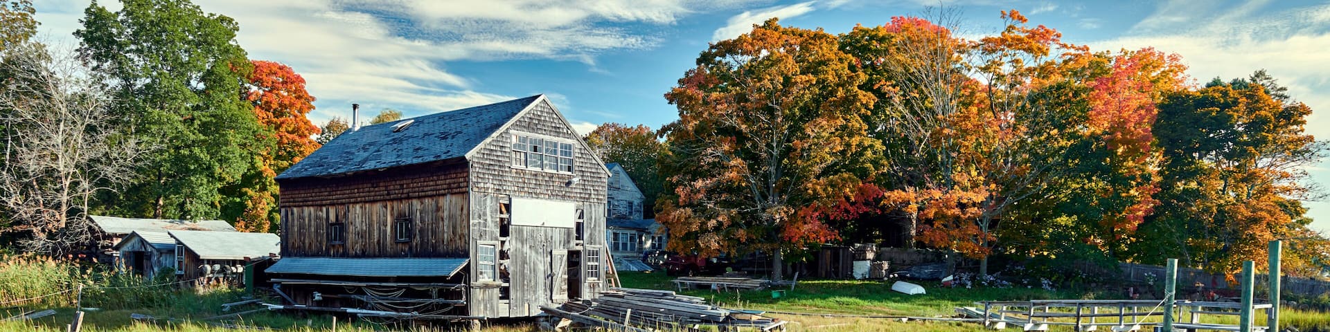 A rustic wooden barn, a calm river, and autumn-colored trees.