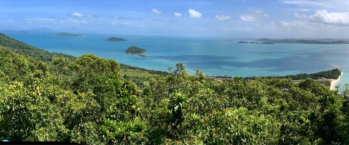 A coastal landscape with lush greenery, clear blue waters, and distant islands.