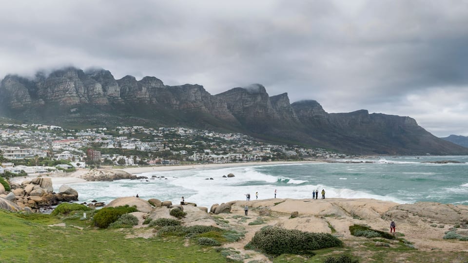 A coastal town with a rugged mountain backdrop, rocky shoreline, and ocean waves.