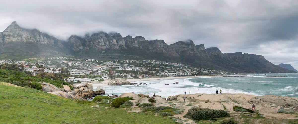 A coastal town with a rugged mountain backdrop, rocky shoreline, and ocean waves.