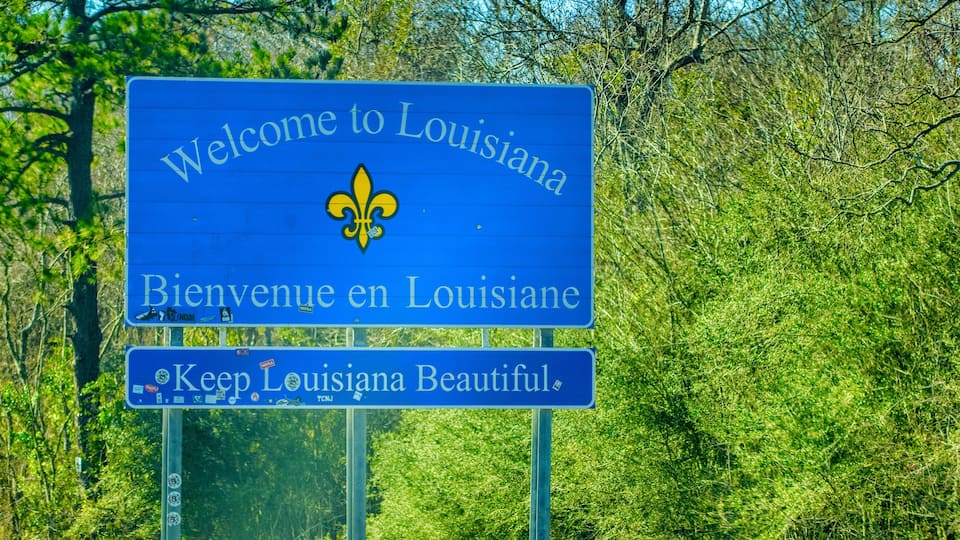 A blue welcome sign with 'Welcome to Louisiana' and a fleur-de-lis emblem.