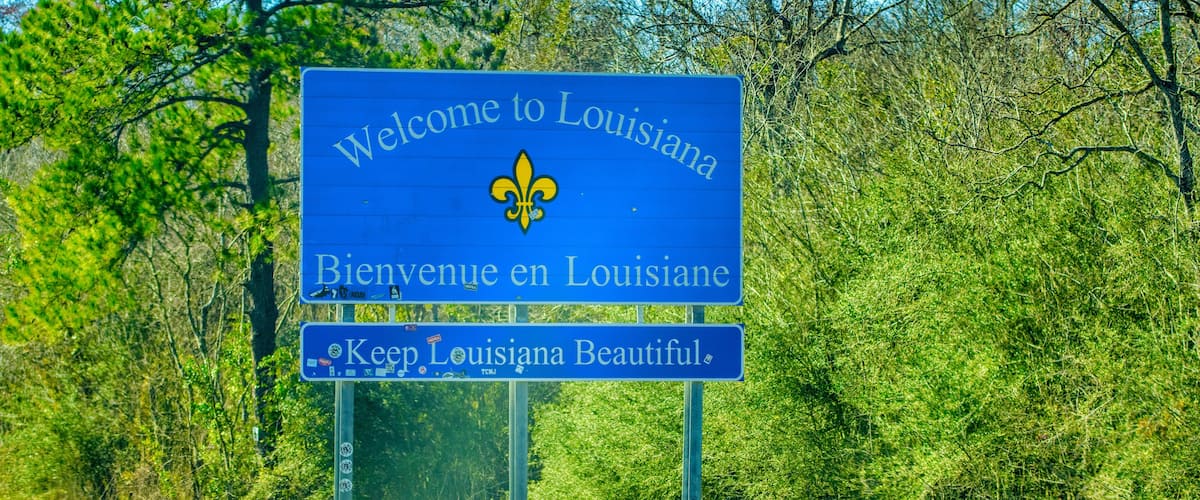 A blue welcome sign with 'Welcome to Louisiana' and a fleur-de-lis emblem.
