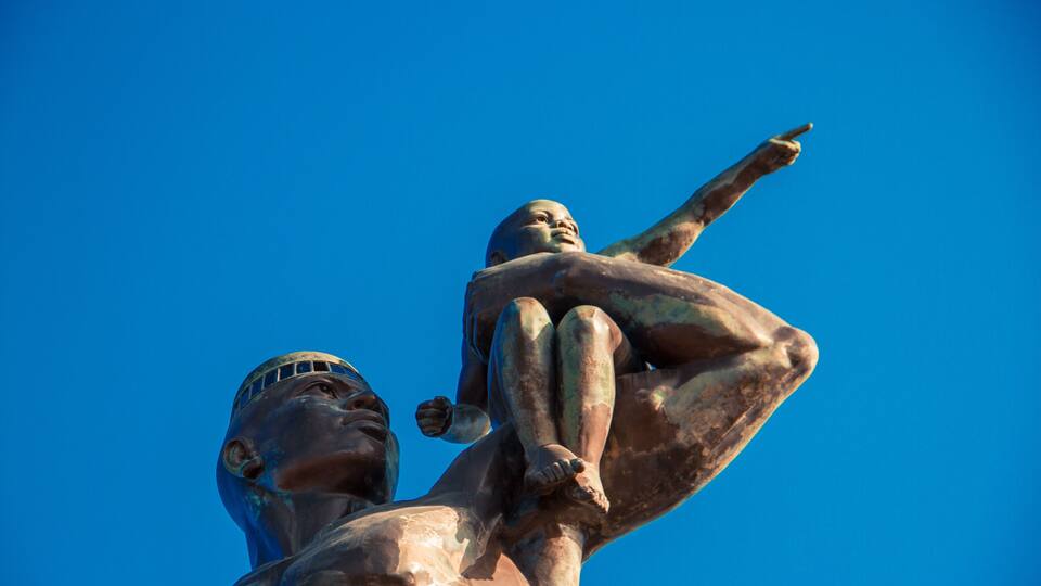 A statue with a child on its shoulders, set against a clear blue sky.