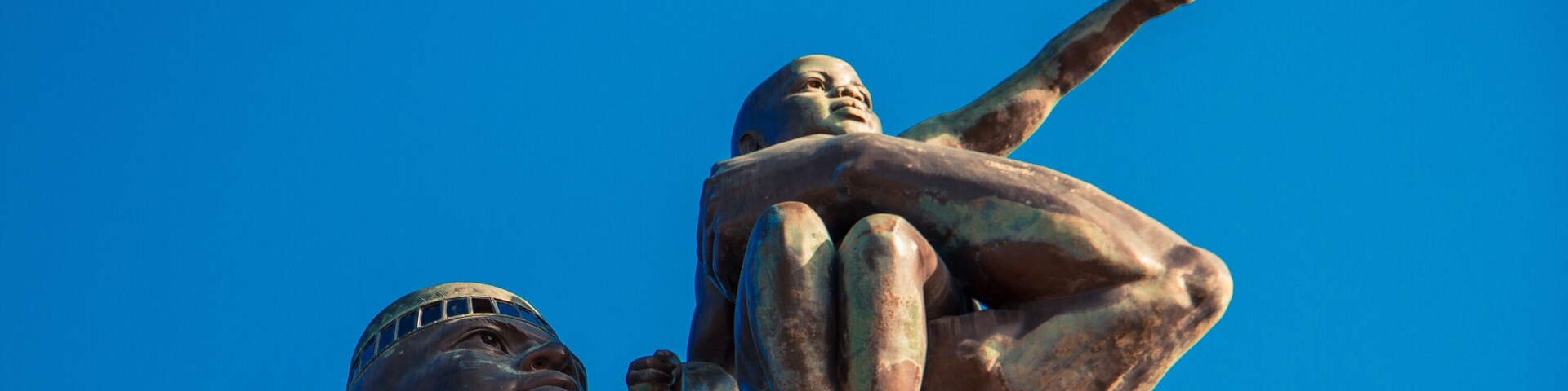 Una estatua con un niño sobre sus hombros, frente a un cielo azul despejado.